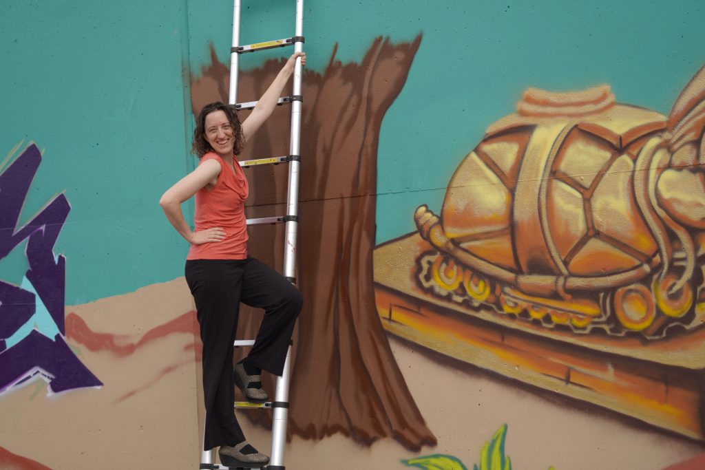 Shelley climbing ladder against a graffiti wall